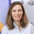 Portrait d'une femme souriante aux cheveux bruns portant une chemise blanche.