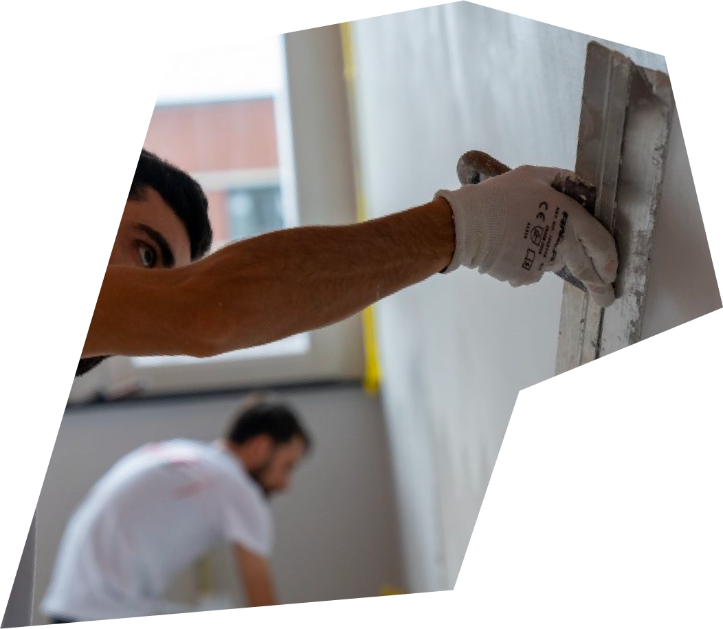 Worker smoothing a wall with a trowel while another person works in the background.