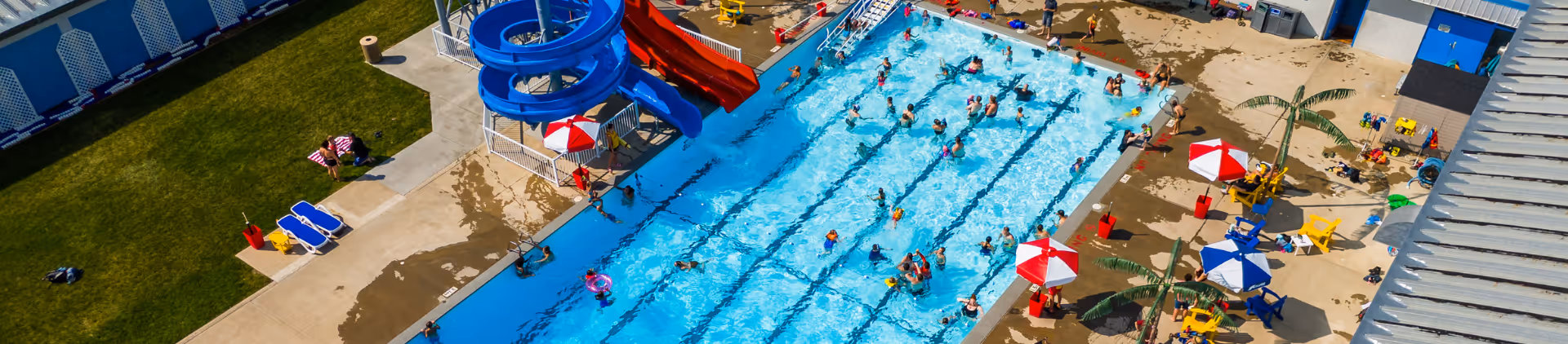 Aerial view of an outdoor pool with many swimmers, water slides, umbrellas, and lounge chairs.