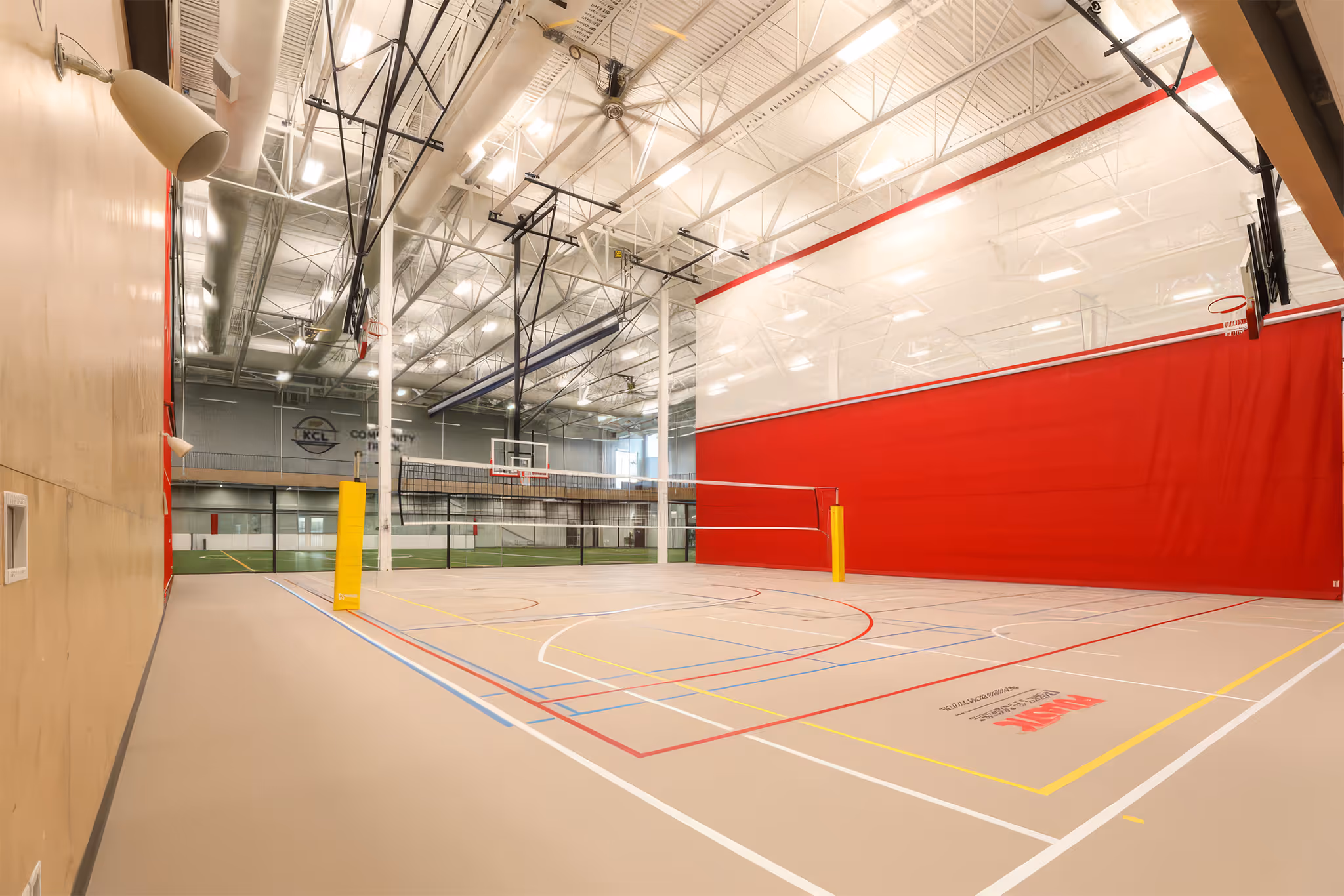 Indoor sports court with a volleyball net, basketball hoops, and marked lines for multiple sports.
