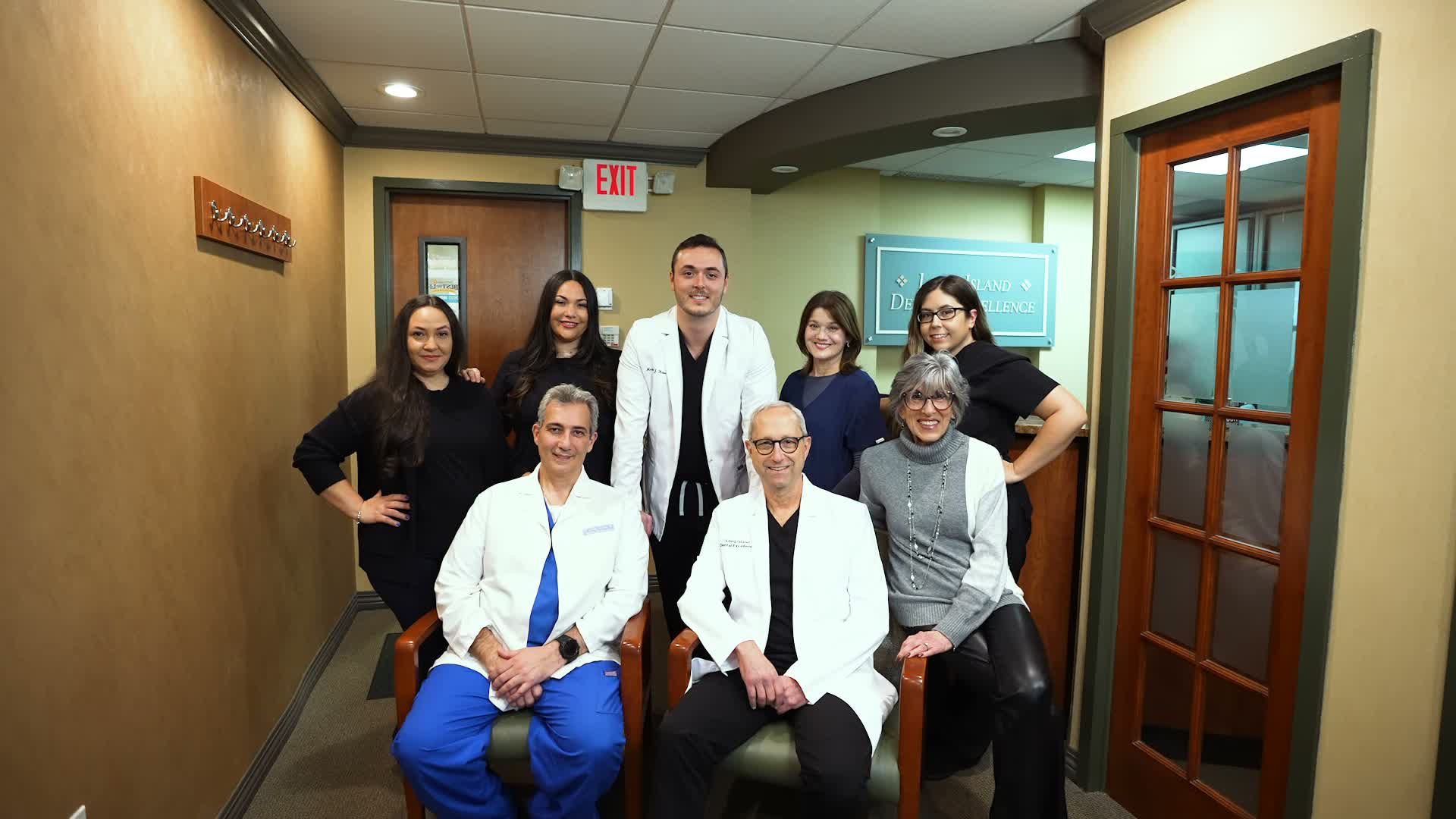 Group photo of eight medical professionals, including three men in white coats seated and five women standing behind them in an office hallway.
