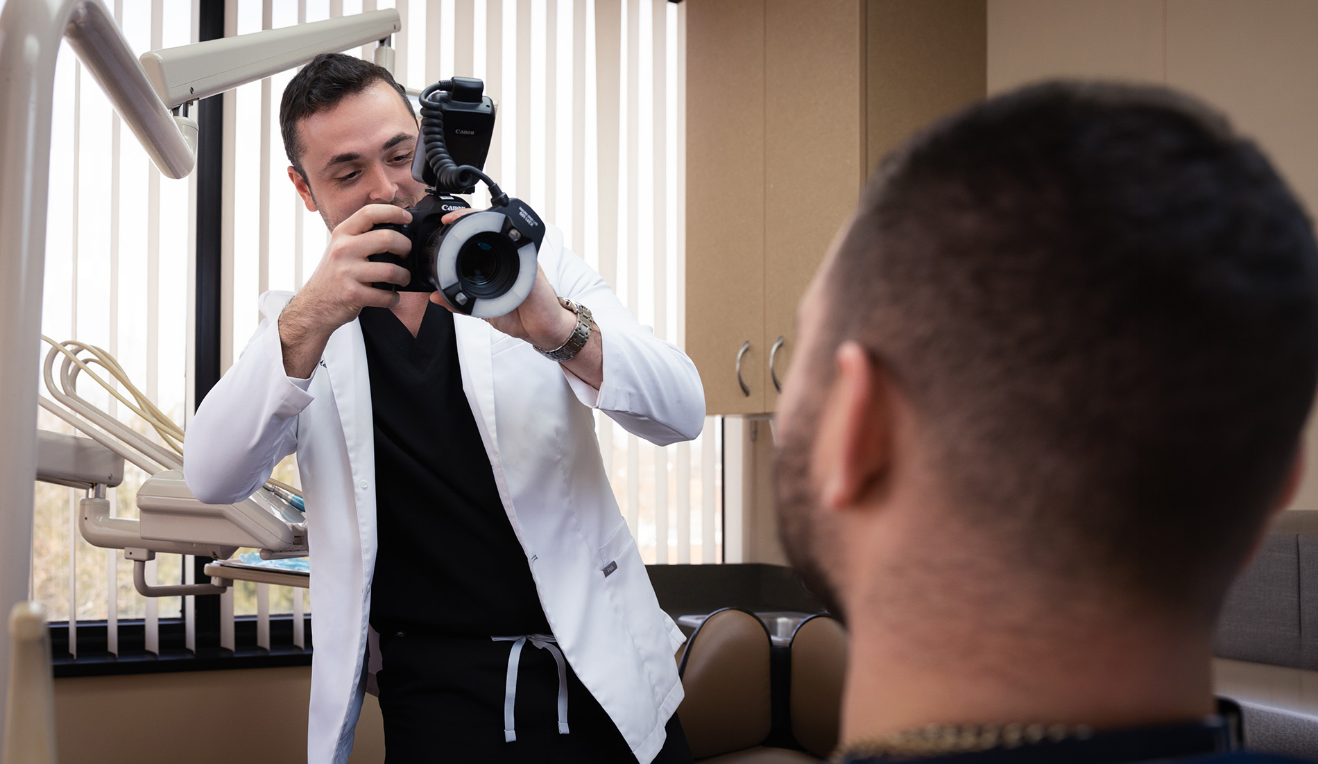 Dentist in a white coat taking a photo of a patient using a professional camera in a dental clinic.