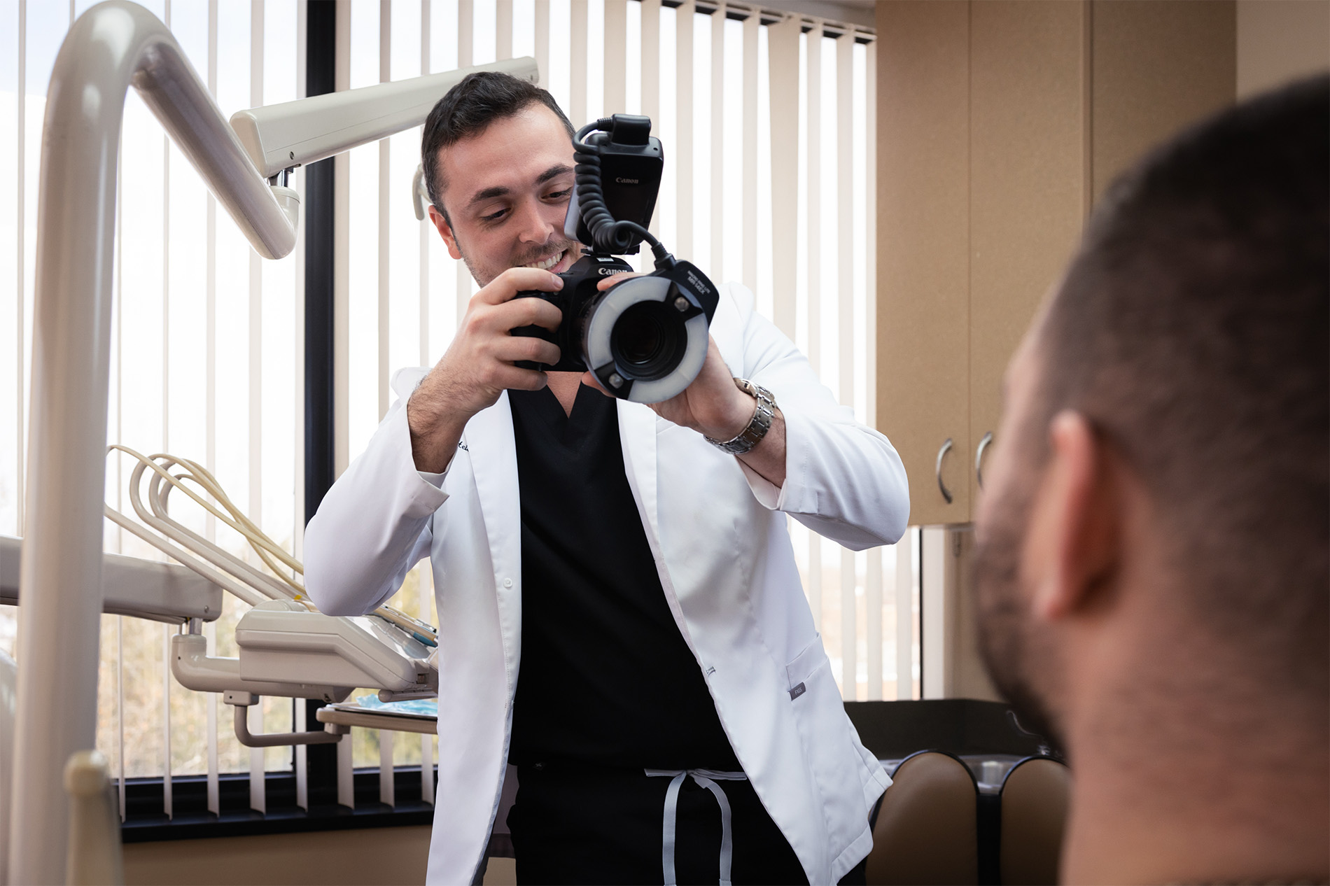 Dentist wearing a white coat taking a photo of a patient's mouth with a professional camera in a dental office.