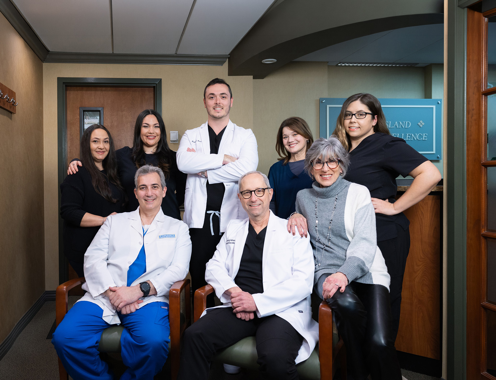 Group of eight healthcare professionals, including doctors in white coats and staff in black scrubs, posing indoors in a clinic setting.