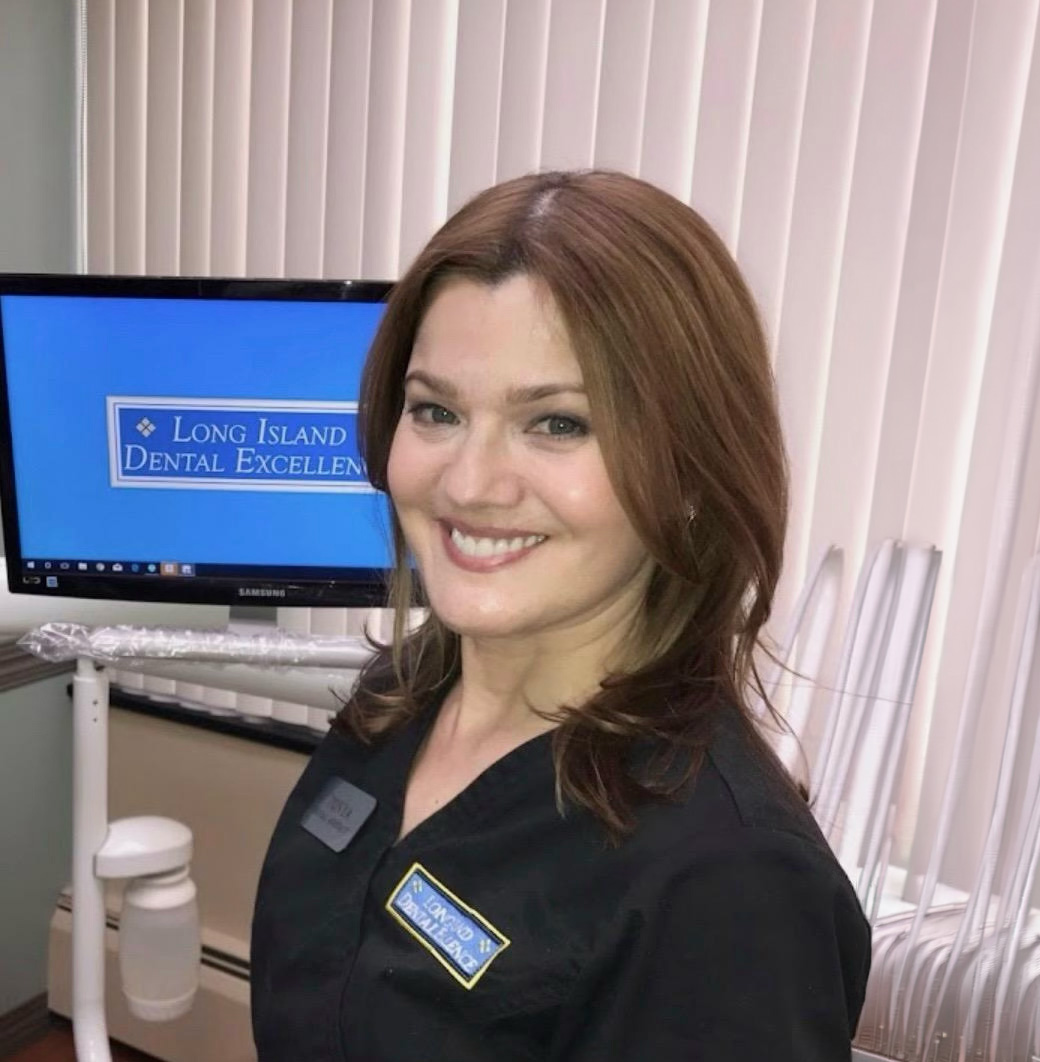 Smiling female dental professional wearing black scrubs with Long Island Dental Excellence logo in a dental office.