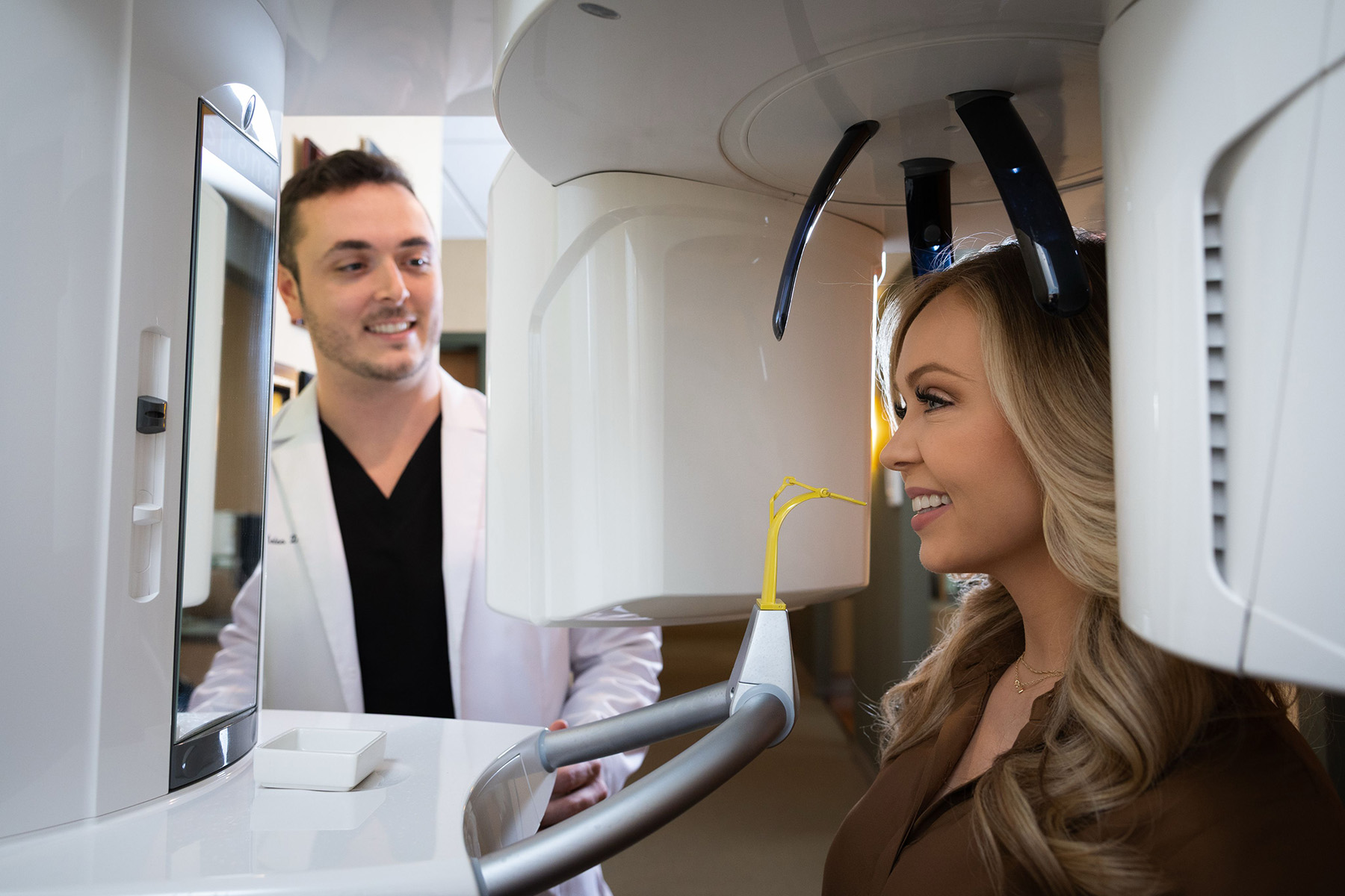 Dentist smiling at a female patient positioned in a dental panoramic X-ray machine.