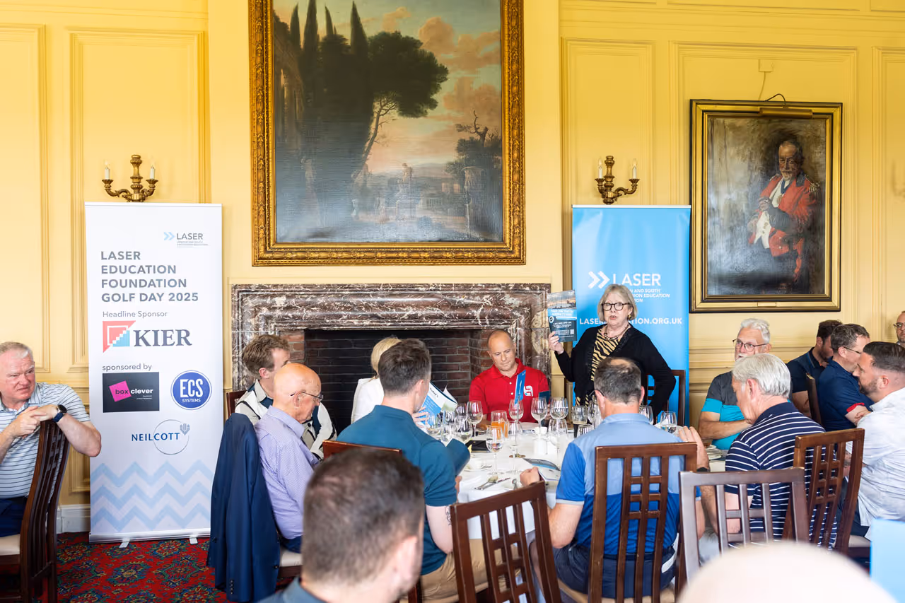 Group of people seated around a dining table in a formal room with yellow walls, attending Laser Education Foundation Golf Day 2025 event.
