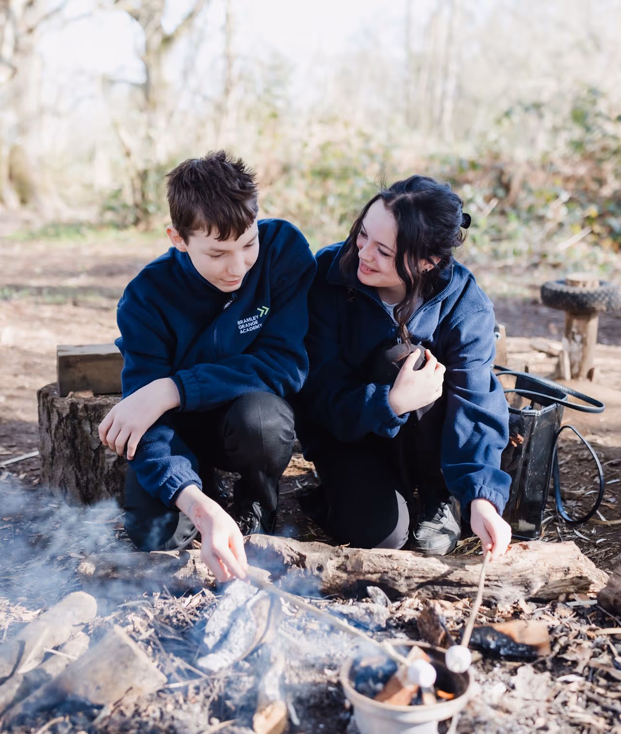 Two children in navy jackets roasting marshmallows over a campfire outdoors.