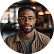 Smiling man with a beard wearing a brown jacket inside a café with blurred background.