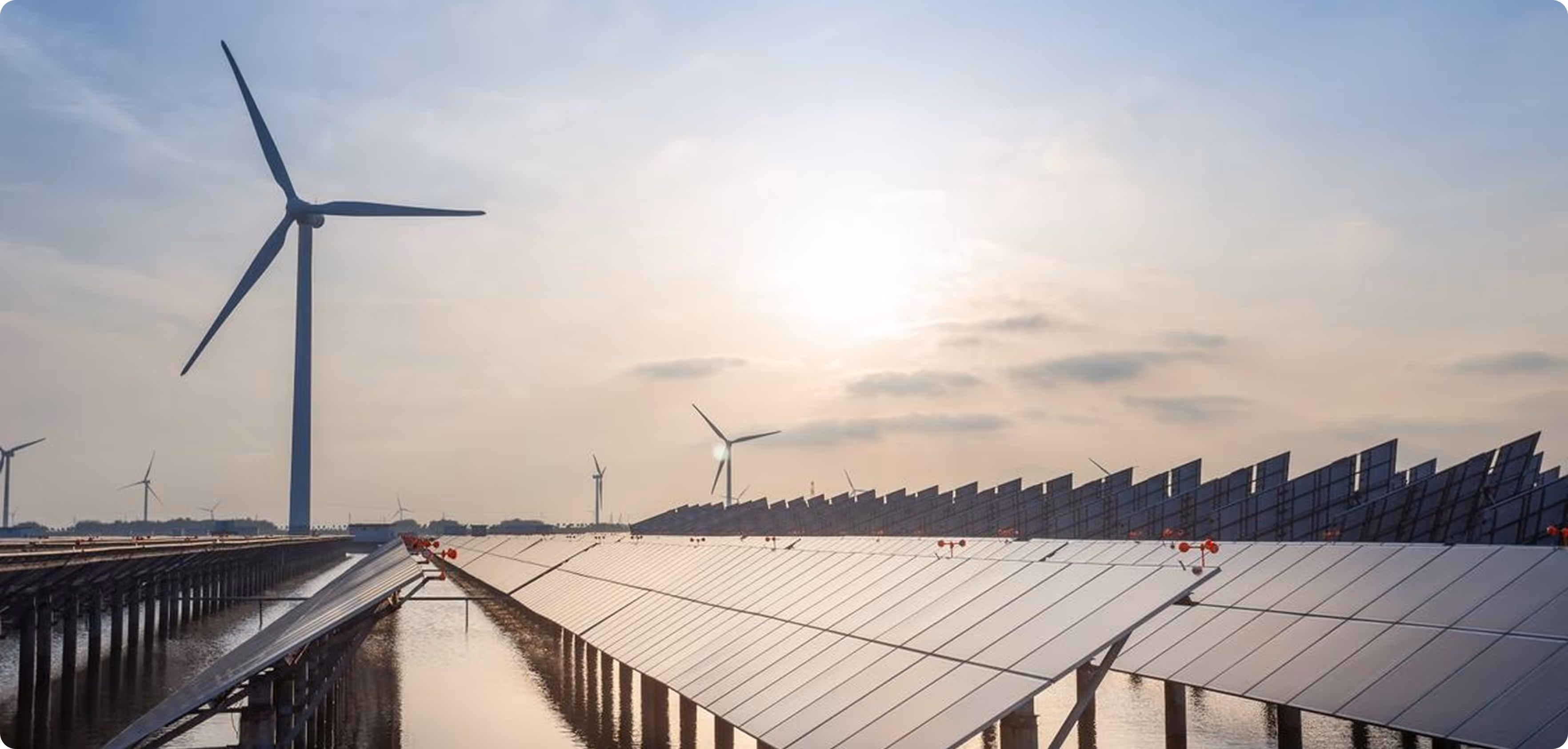 Solar panels over water with wind turbines in the background at sunset.