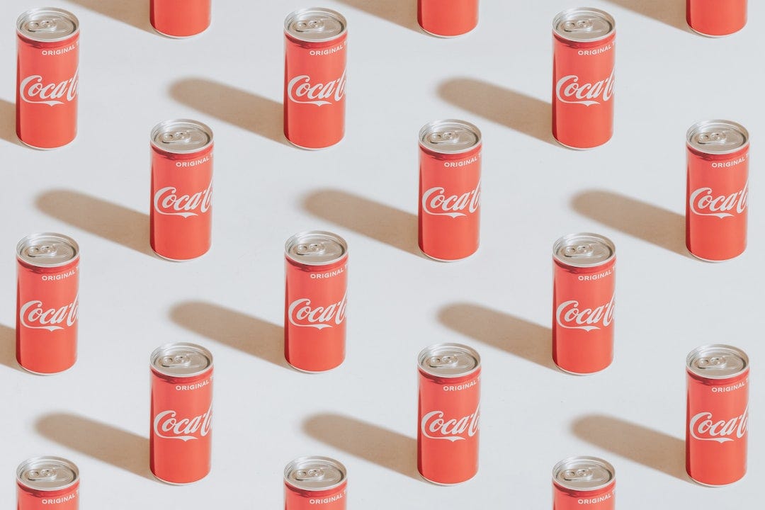 Rows of red Coca-Cola cans casting shadows on a light background.