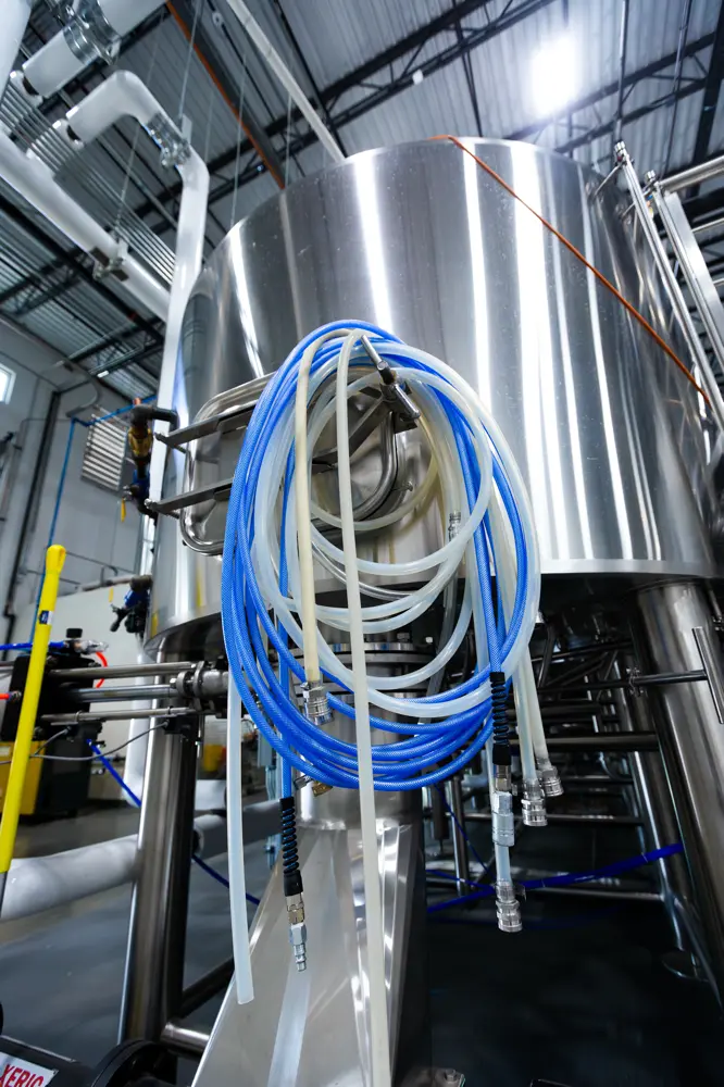 Coiled blue and white hoses hanging on a stainless steel industrial tank in a factory setting.