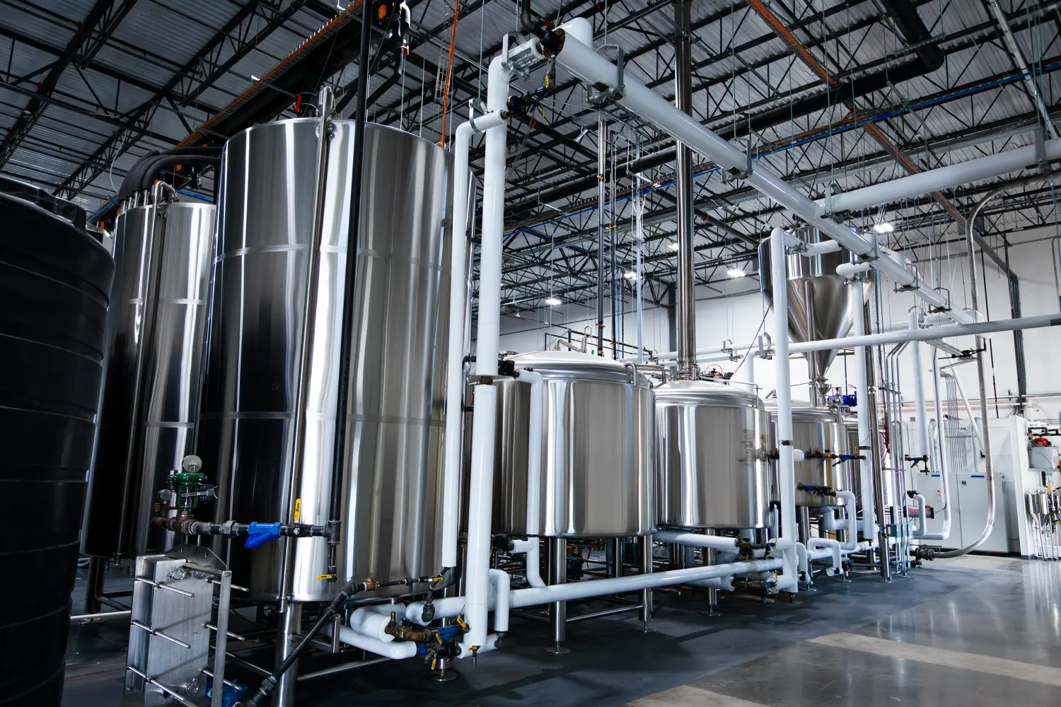Row of large stainless steel industrial tanks connected by white pipes in a factory setting.