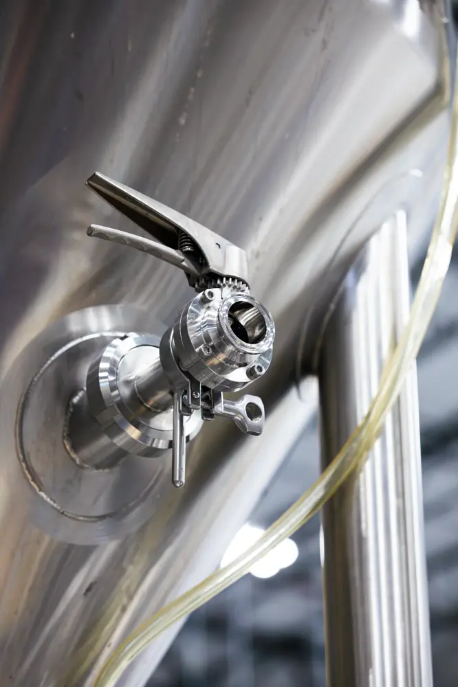 Close-up of a stainless steel valve attached to a fermentation tank with a transparent hose connected, used in brewing or industrial processes.