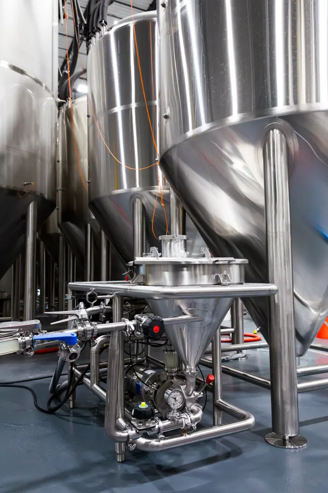 Large stainless steel fermentation tanks and connected pipes in a modern brewery or food processing facility.