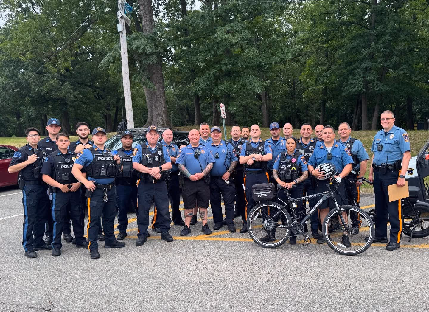 Group of police officers standing together outdoors, some in uniform and one holding a bicycle helmet.
