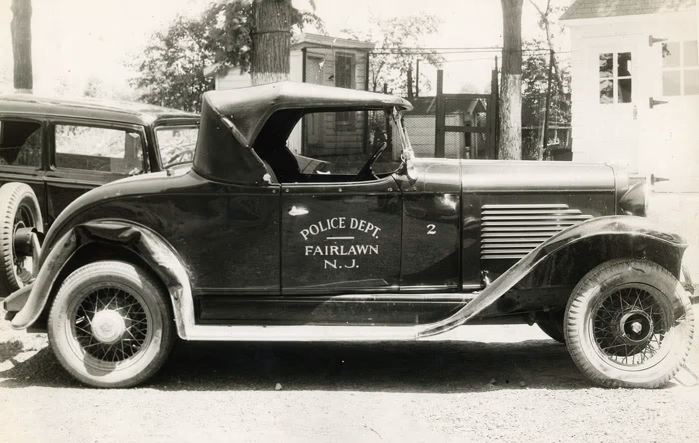 Vintage black police car from Fairlawn, New Jersey, parked outside near a building.