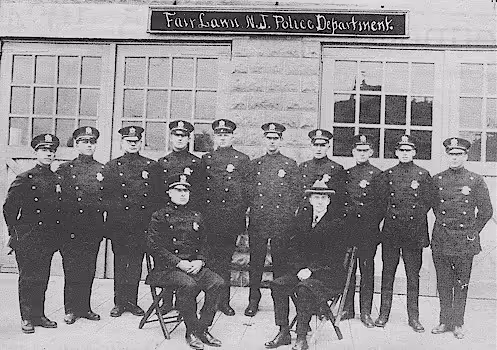 Black and white photo of eleven uniformed police officers posing outside Fairfax N.J. Police Department building, two seated and nine standing.
