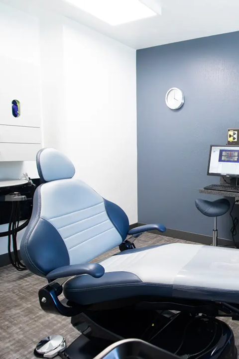 Modern dental examination chair in a clean dental office with a clock and computer monitor in the background.