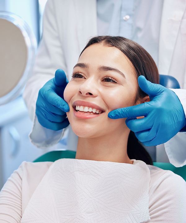 Dentist wearing blue gloves examining the smiling woman's teeth in a dental office.
