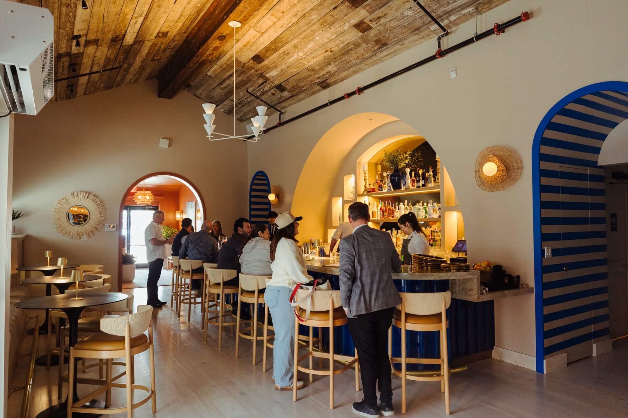 Guests gather at Meraki's tiled blue bar beneath warm archways lined with spirits and Mediterranean decor.