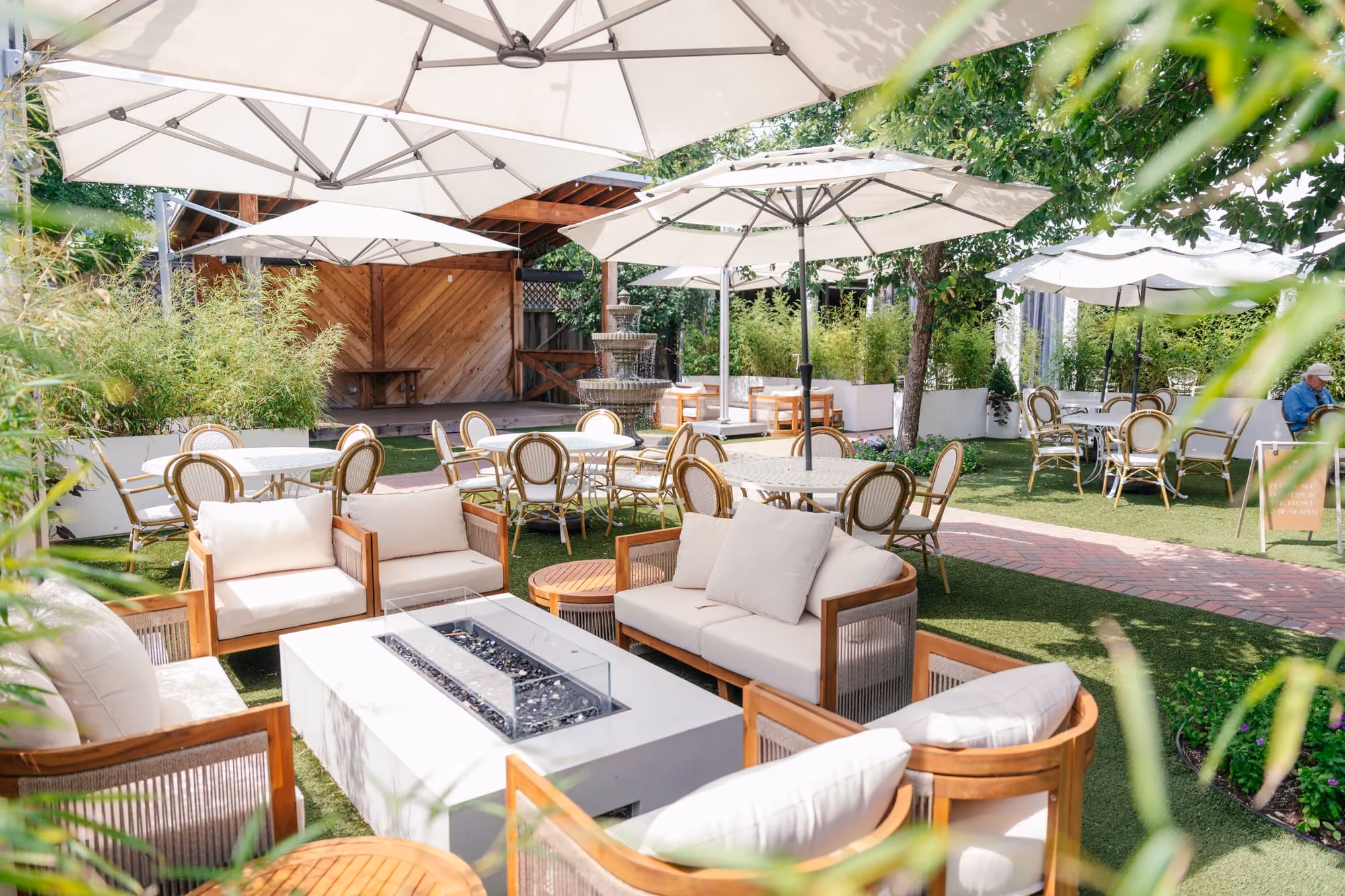 The Courtyard at Meraki features shaded lounge seating, a fire pit, and open-air dining around a stone fountain.