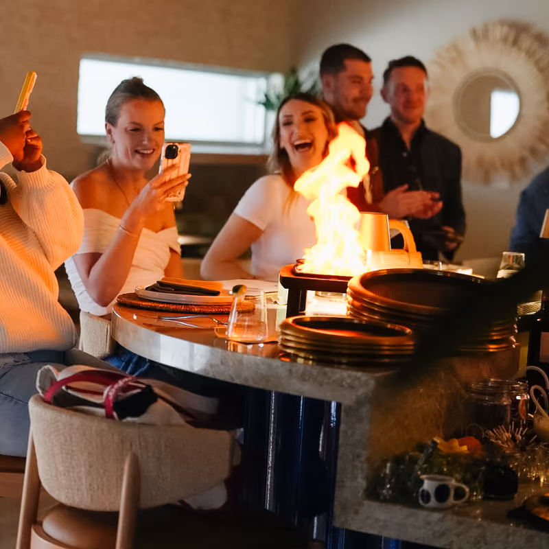 Guests laughing as a flaming dish is fired tableside at a Meraki event