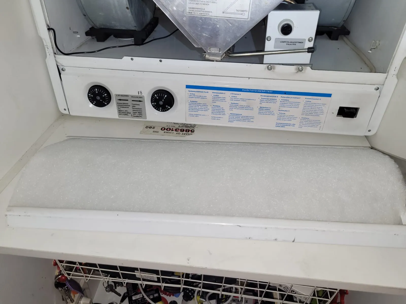 Valkoinen ilmanvaihtokone, jossa näkyy suodatin, säätönupit ja huolto-ohjeet. Valoisa ja selkeä kuva.