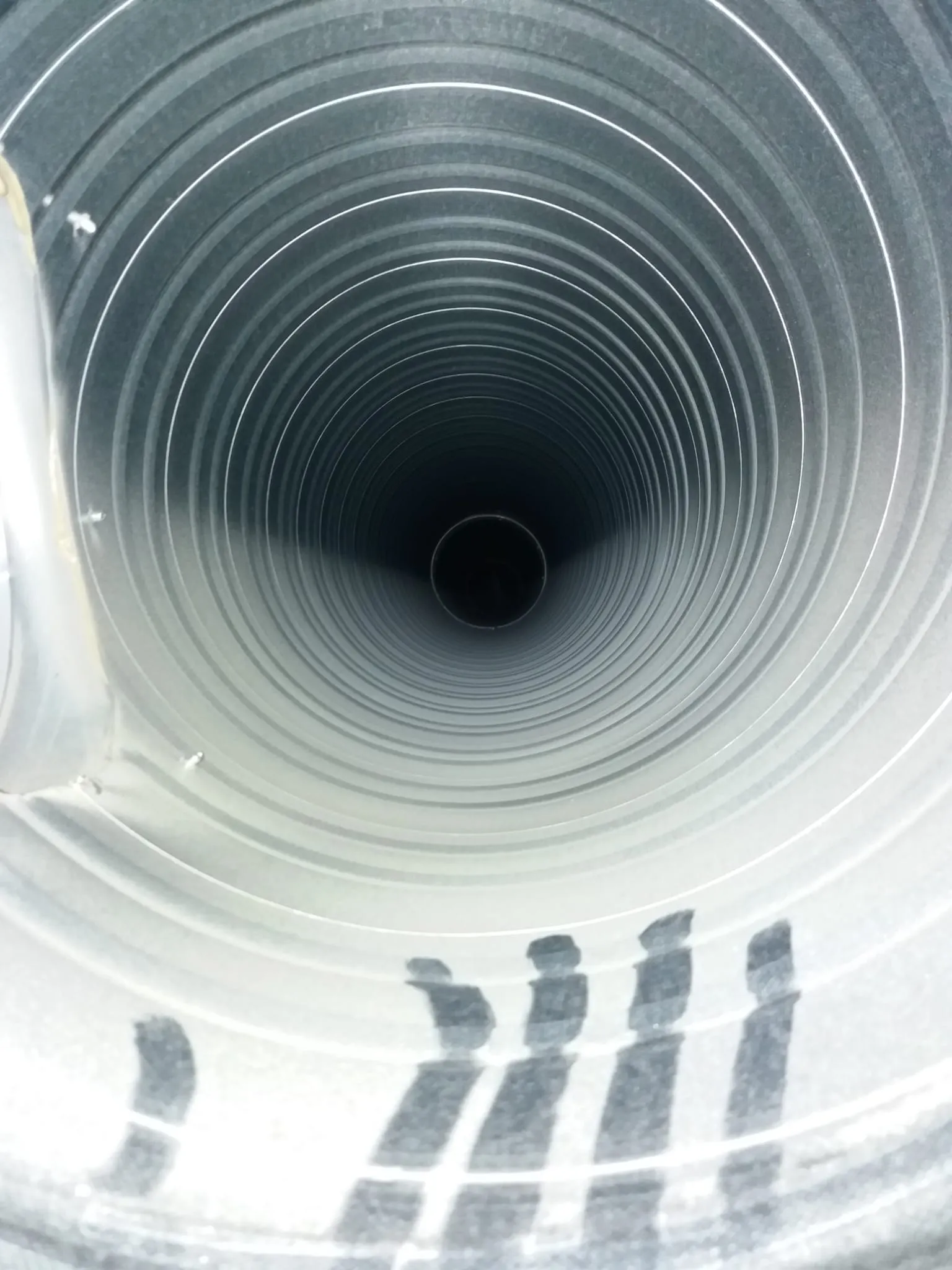 Metallinen, aaltoileva putki, jossa on tumma aukko päässä ja harmaita merkintöjä pohjalla, valaistus on kirkas ja tasainen.