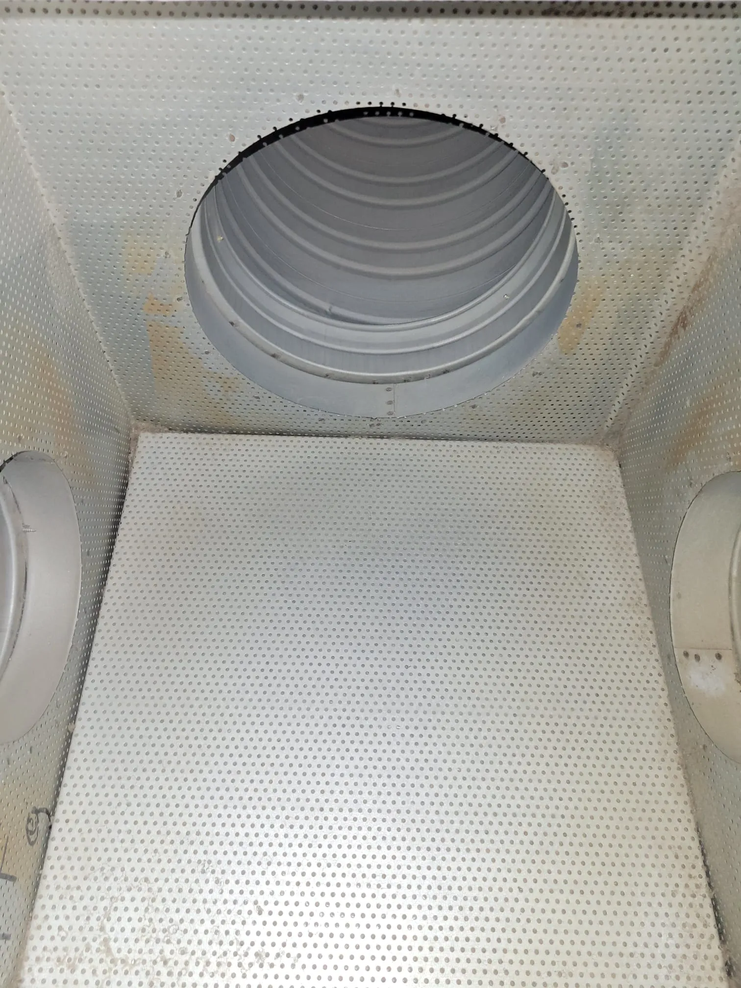 Metallinen, rei'itetty sisätila, jossa on pyöreä aukko ylhäällä ja kaksi putkea sivuilla, valaistus on tasainen.