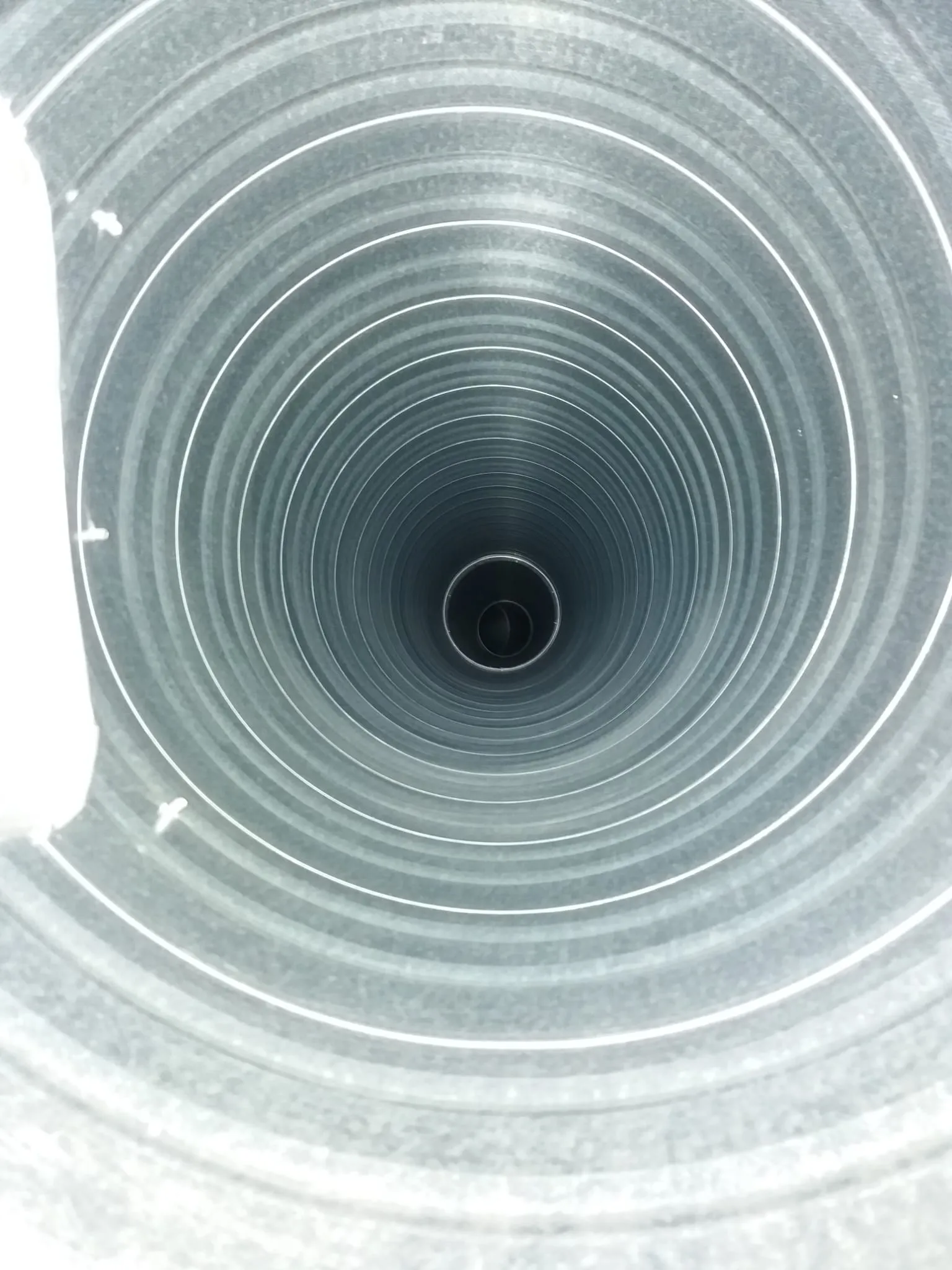 Kuva metallisesta putkesta, jossa on ympyröitä ja tumma aukko keskellä, valaistus on epätasainen.