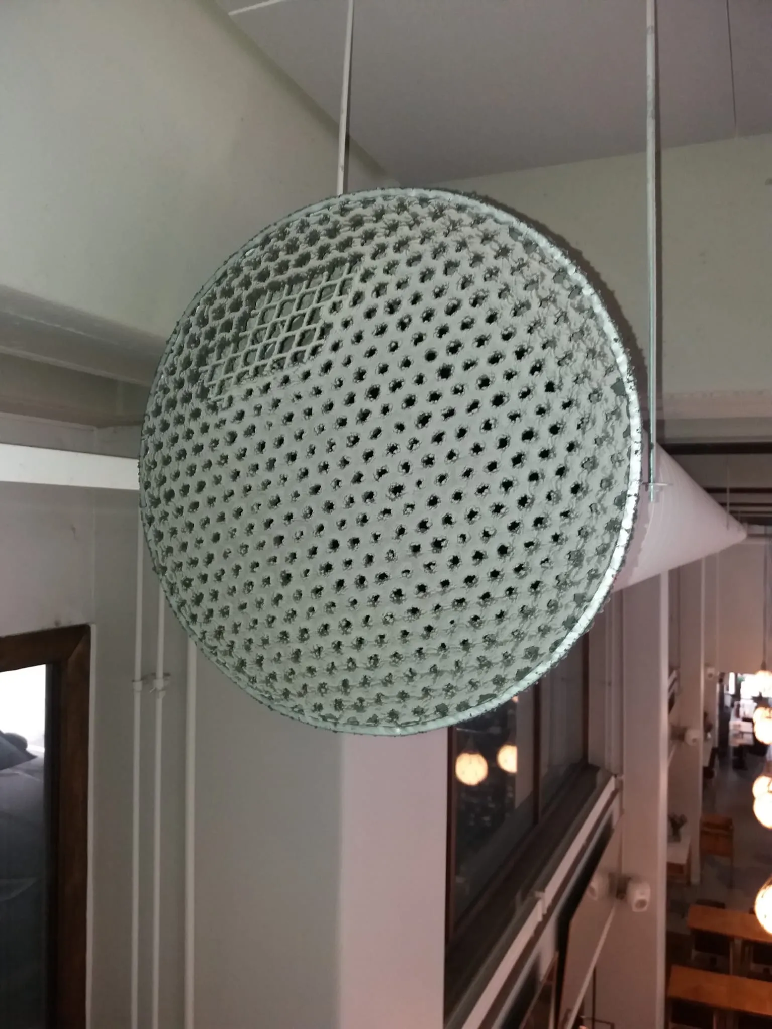 Kattoon ripustettu pyöreä, rei'itetty valaisin, jossa on metallinen kehys ja valkoiset ripustusvaijerit.