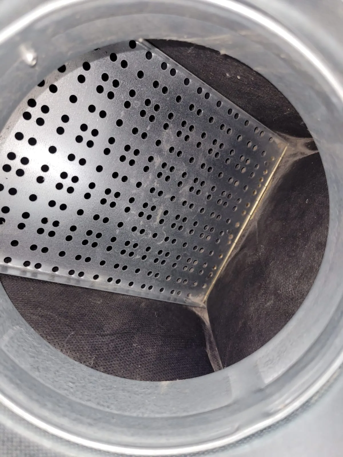 Metallinen putki, jossa on rei'itetty metallilevy ja tumma kangas sisällä, valaistus on kirkas.