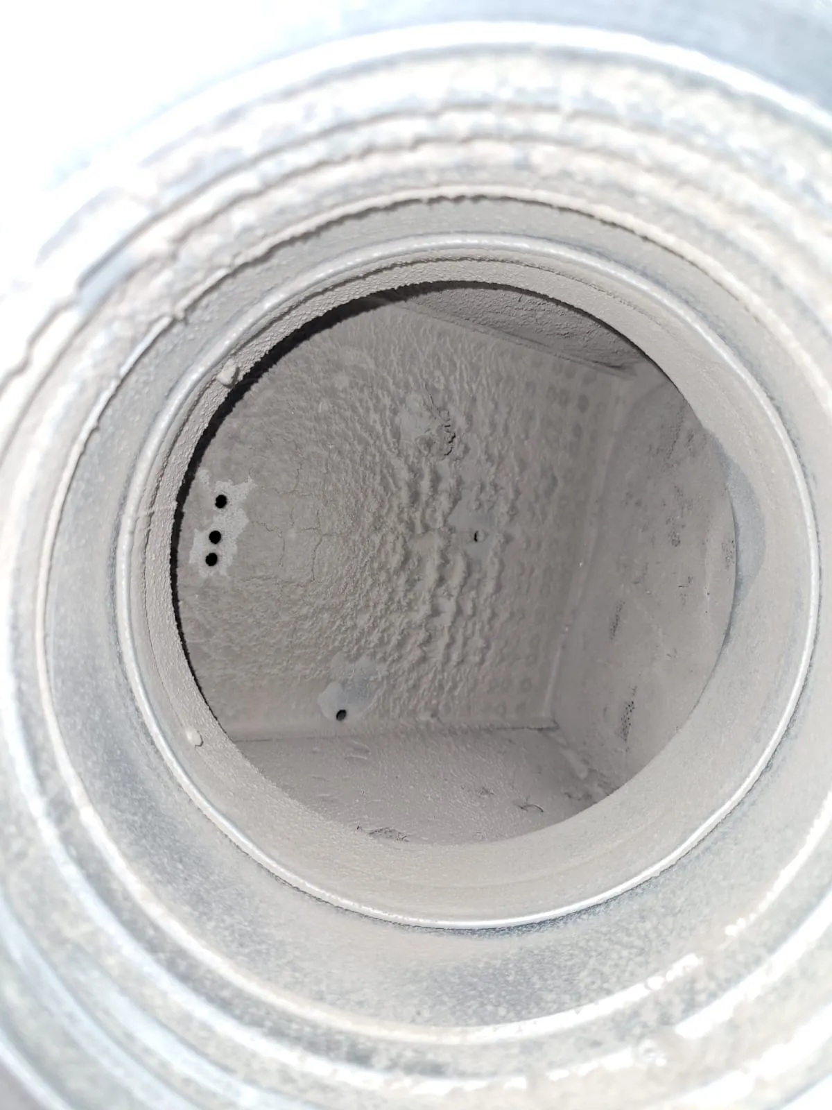 Metallinen, pyöreä ilmastointikanava, jossa on paljon pölyä ja likaa sisäpuolella, valaistus on himmeä.