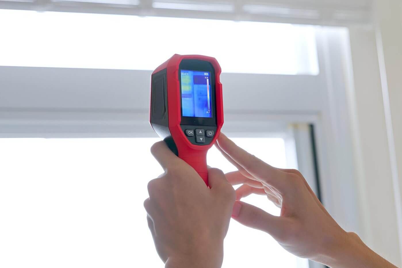 Punainen lämpökamera kädessä, ikkuna taustalla, sininen näyttö.