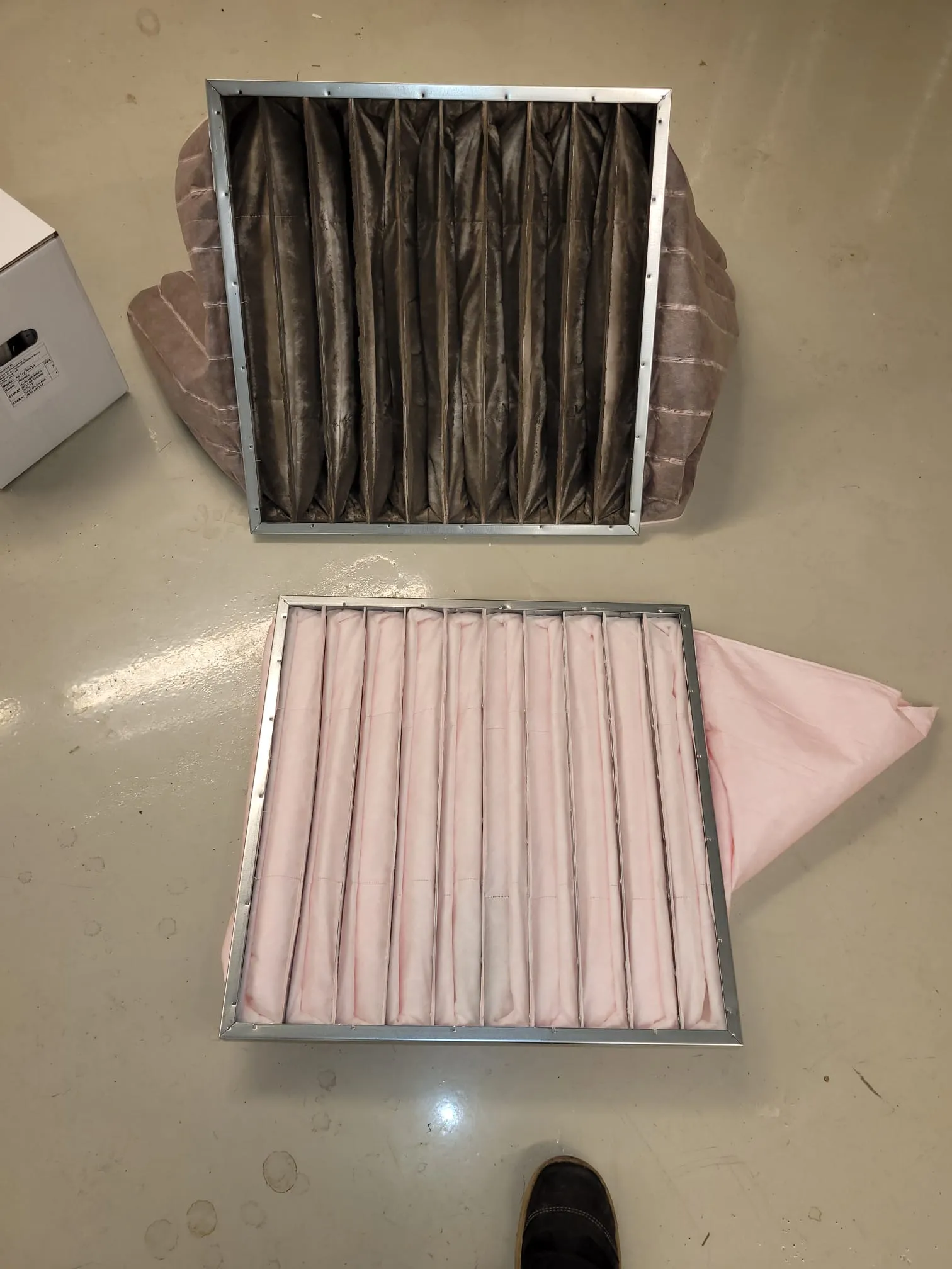 Kaksi suodatinta, toinen likainen ja toinen puhdas, vaalealla lattialla, jossa on pehmeä valaistus.