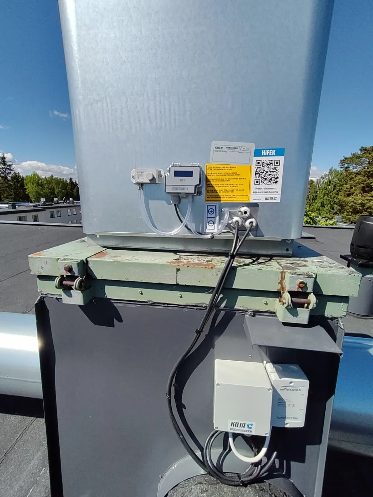 Ilmakanava katolla, jossa on mittalaitteita, putkia ja sähköjohtoja aurinkoisena päivänä.