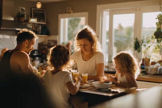 Family of four having breakfast together in a sunlit kitchen.