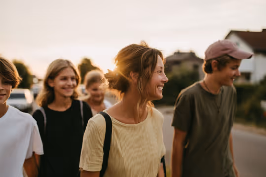 Group of smiling teenagers walking outside on a sunny day with houses in the background.