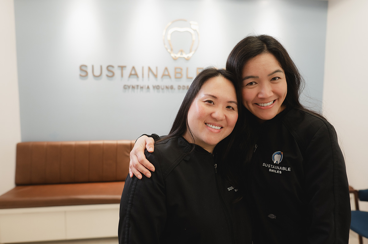 Two female dental professionals hugging, smiling at camera in office