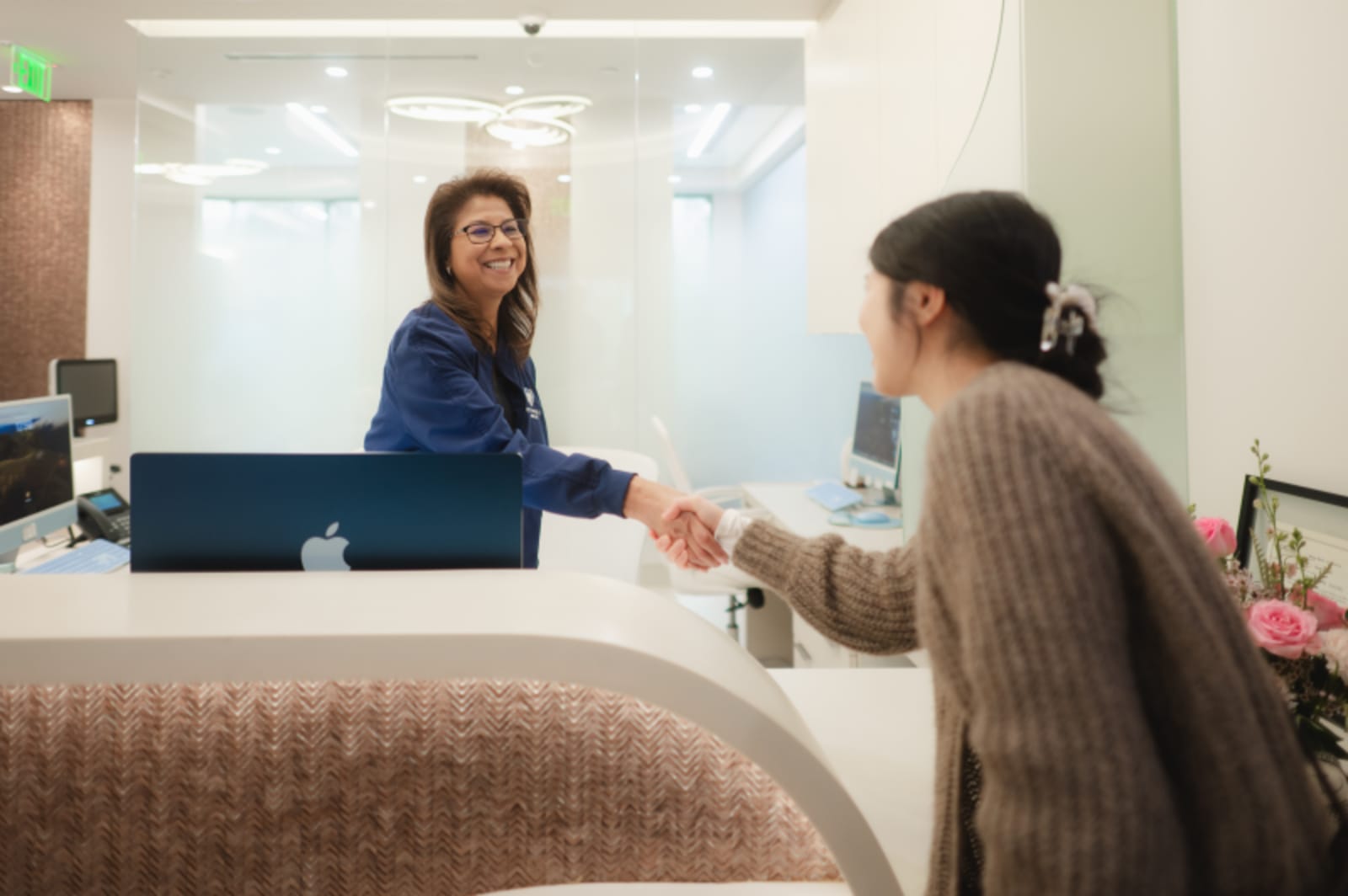 Female dentist greeting and smiling with patient at reception desk