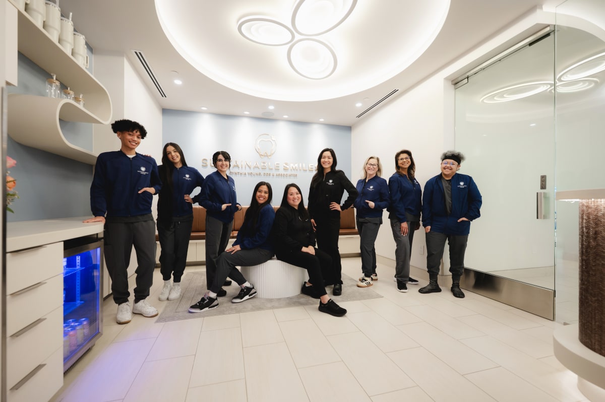 Dental team and patients gathered in a modern, bright treatment room at Sustainable Smiles