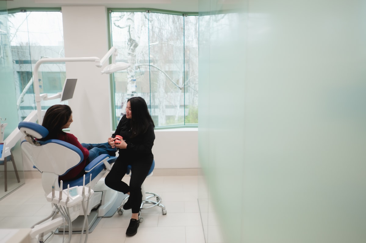 Female dentist showing pink dental model to young patient in clinical setting