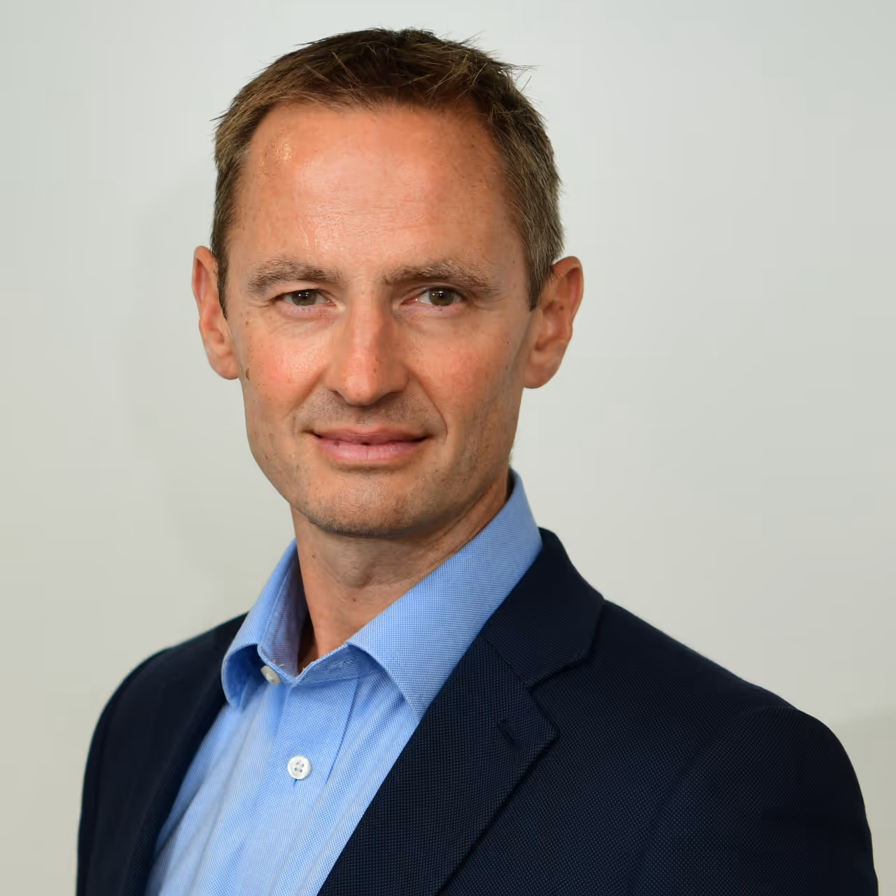 Portrait of a middle-aged man wearing a blue shirt and dark blazer against a plain light background.
