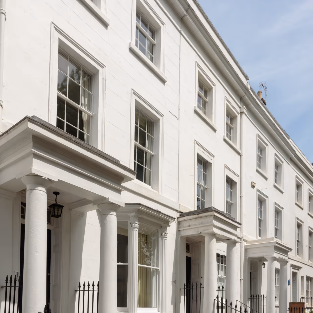 Row of white Georgian-style townhouses with tall columns and multiple windows under a partly cloudy sky.
