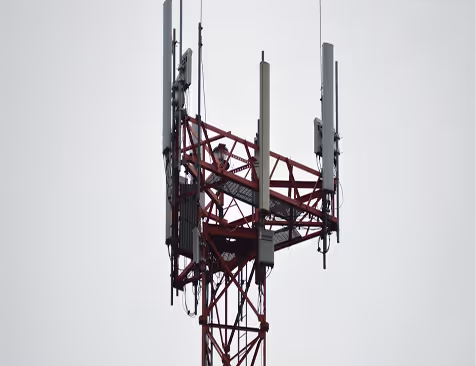 Gornji deo crveno-belog telekomunikacionog tornja sa antenama na pozadini sivog neba.