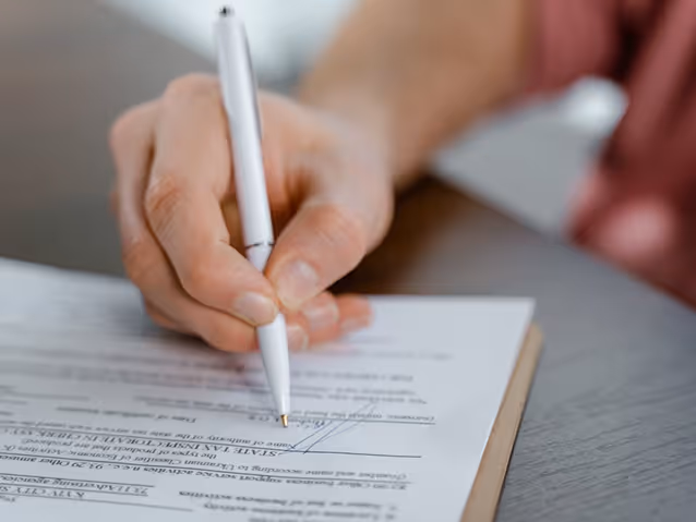 Close-up of a hand holding a pen and signing a document on a clipboard.
