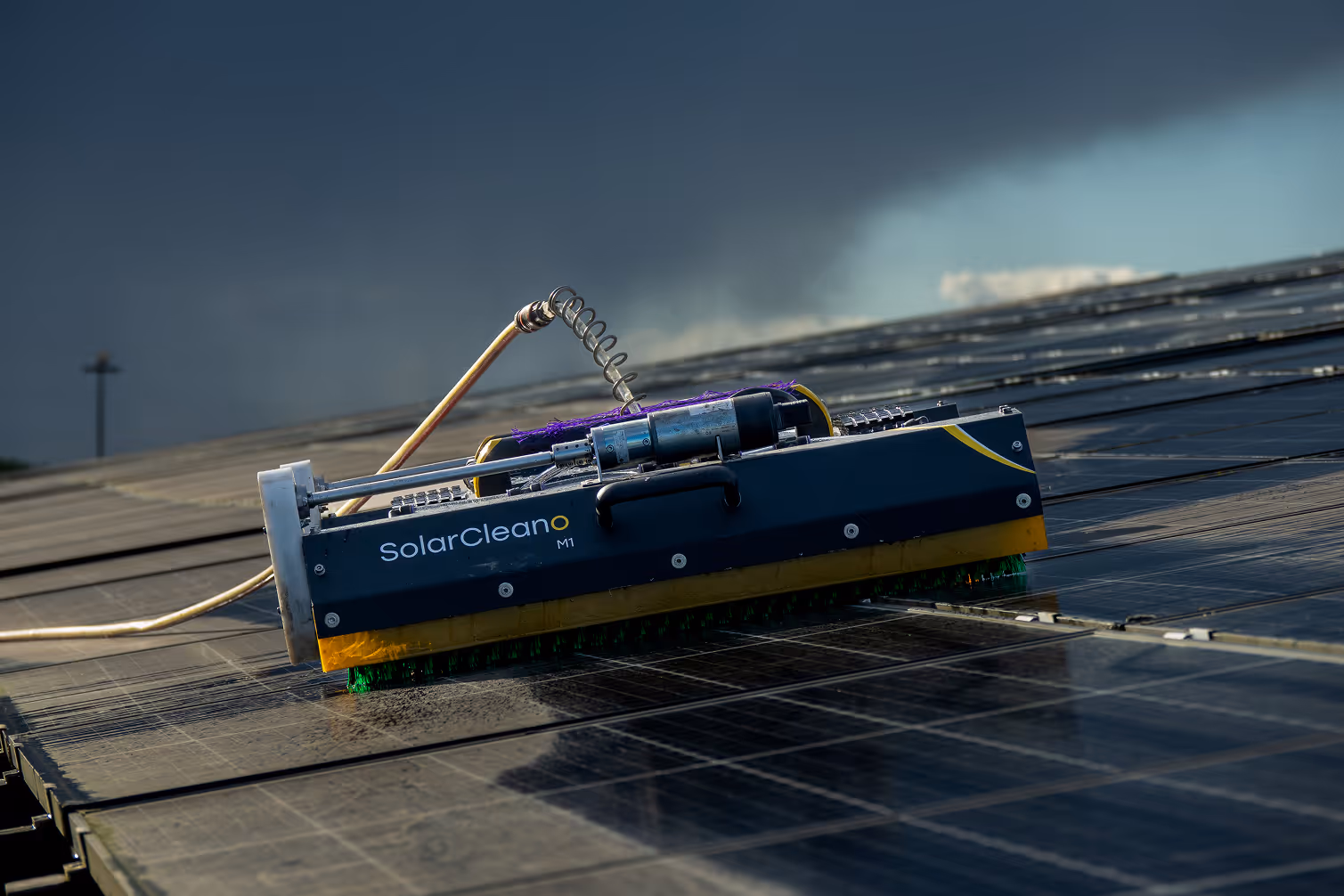 Solar panel cleaning robot named SolarCleano M1 on solar panels under a dark cloudy sky.