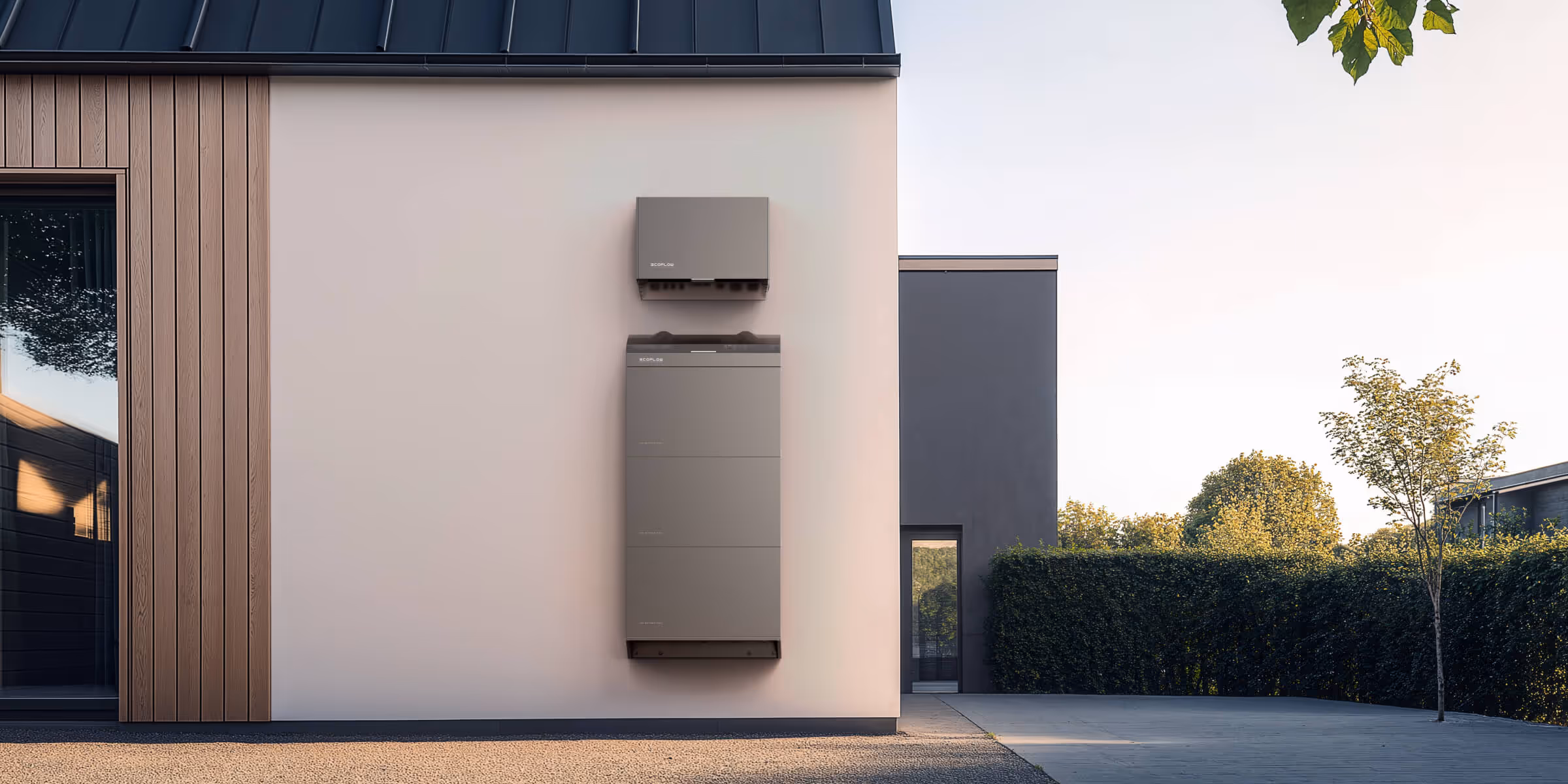 Two gray rectangular battery units mounted on a modern house exterior wall near a door and window.