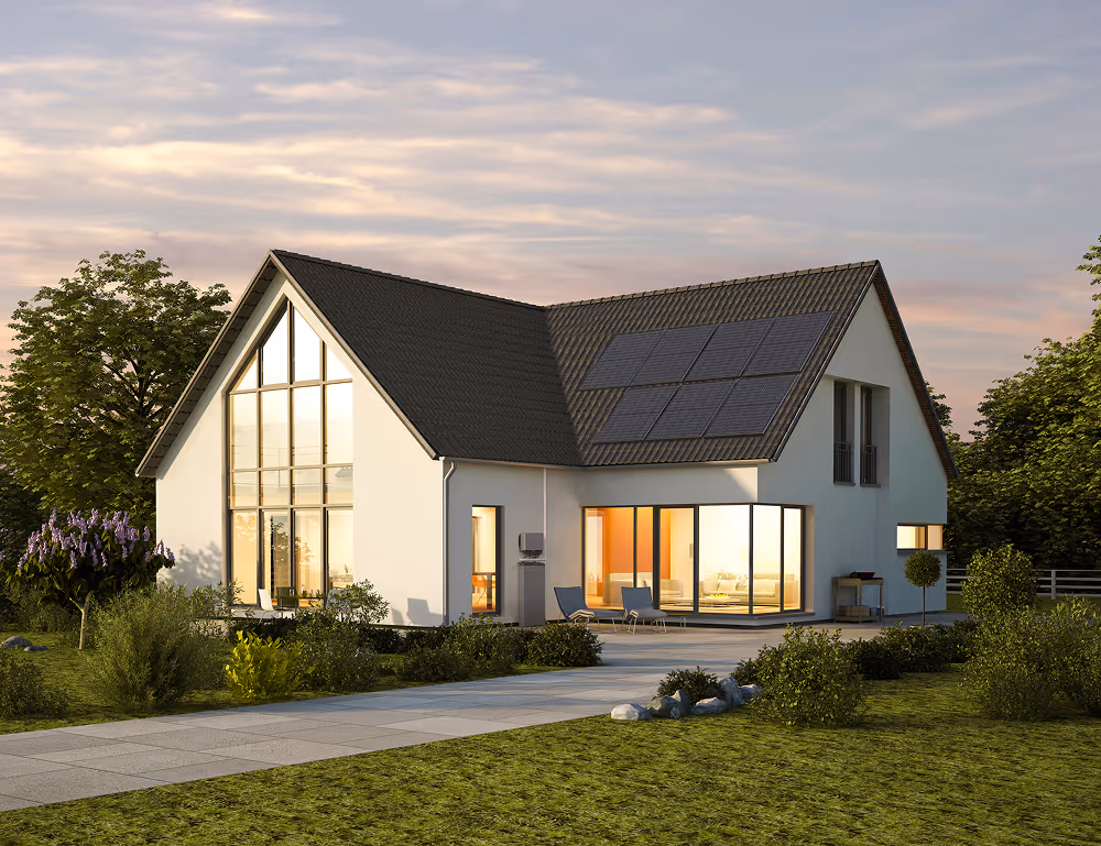Modern white house with large windows, solar panels on roof, and landscaped garden at sunset.